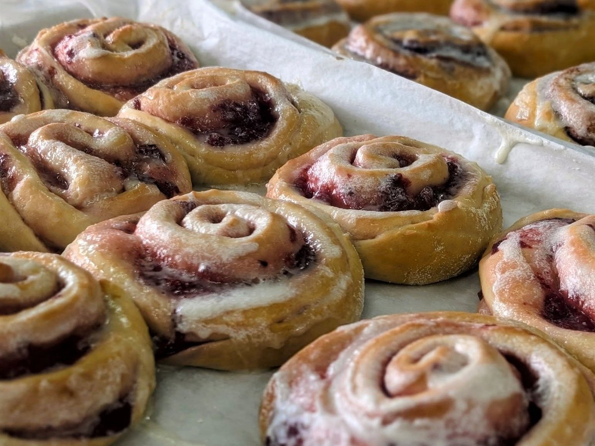 Glazed berry sweet rolls cooling on parchment-lined trays